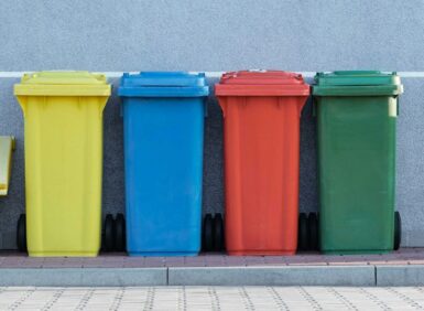 four assorted-color trash bins beside gray wall