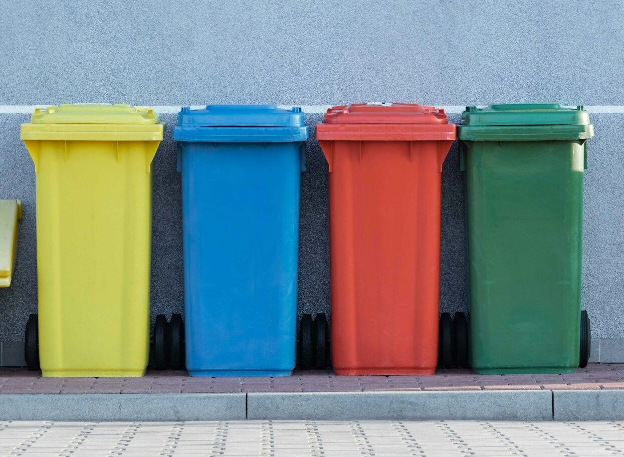 four assorted-color trash bins beside gray wall